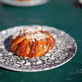 En gyllene kanelbulle med pärlsocker på en mönstrad tallrik. Perfekt för fika, kanske inspirerad av ett enkelt kanelbullar recept.
