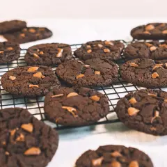 Många mörka, veganska chocolate chip cookies med chokladbitar ligger på ett svart galler.