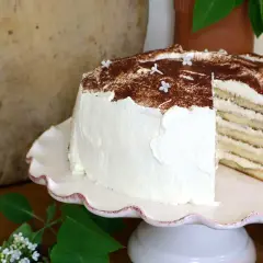 En vacker tiramisu tårta med lager av kräm och kex, toppad med kakao och små vita blommor.
