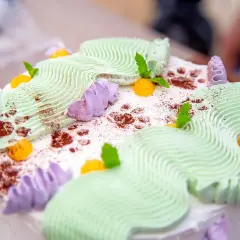 En vacker jordgubbsmousse tårta med grön och lila frosting, toppad med aprikoser och myntablad.
