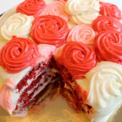 En saftig red velvet-tårta med lager av rött och vitt fluffigt frosting, dekorerad med rosformade frostingblommor i rött och vitt.