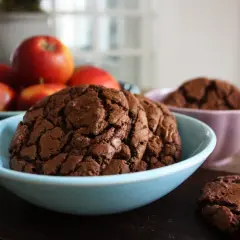 Mörka, sega kladdkake cookies i en ljusblå skål, med äpplen i bakgrunden. En perfekt fika!