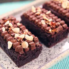 Mörka, saftiga glutenfri brownie bitar toppade med chokladfrosting och nötter på ett marmorerat fat.