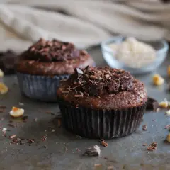 Två chokladmuffins med nutella och strössel av choklad. Hasselnötter och chokladbitar ligger utspridda runt dem.