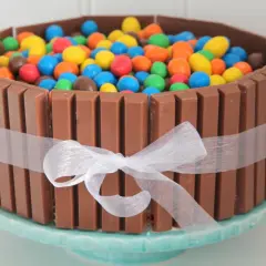 En färgglad KitKat tårta fylld med M&M's, omgiven av KitKat-bars och ett vitt sidenband. En dröm för alla godisälskare!