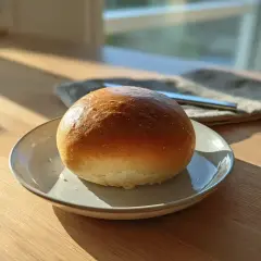 En gyllene, fluffig bulle ligger på en tallrik. Solen lyser in genom fönstret och skapar ett vackert ljus.
