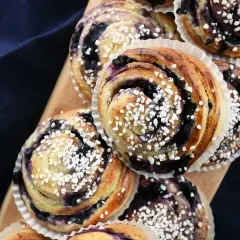 Nybakade blåbärsbullar med pärlsocker på en träbricka, redo att avnjutas.