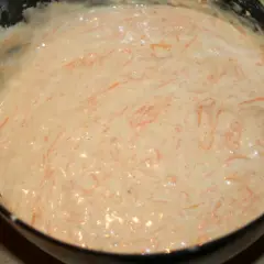 En skål med poröst smör och socker, blandat med rivna morötter. En spatel rör om i smeten.
