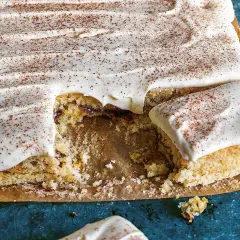 En saftig sockerkaka med krämig glasyr och ett generöst strössel av kanel. En bit saknas, redo att avnjutas.