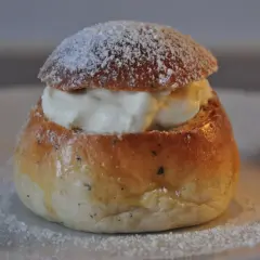 En nybakad semla, redo att avnjutas. Den gyllene bullen är fylld med fluffig grädde och pudrad med florsocker. Perfekt för att baka semmelbullar.