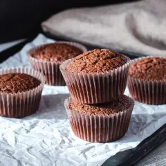 Fem choklad cupcakes i pappersformar, staplade och utspridda på vitt papper.