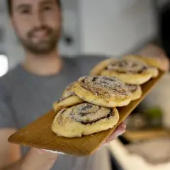 Man håller fram en bricka med nybakade kanelbullar utan ägg, strösslade med socker.
