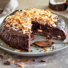 En saftig brownie med chokladglasyr och rostad kokostosca. En sked med chokladsås ligger bredvid.