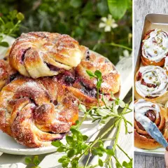 Fyllda bullar med bär och socker på en vit tallrik, bredvid en plåt med kanelbullar med glasyr och pistagenötter.