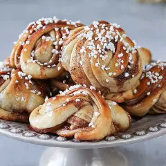 En hög med laktosfria kanelbullar, toppade med pärlsocker, ligger på ett fat.