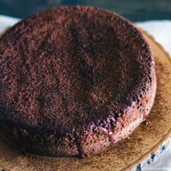 En saftig glutenfri chokladkaka, pudrad med kakao och med smält choklad som rinner ner längs kanten.
