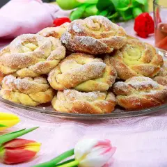 En tallrik med nybakade bullar, perfekt för att doppa bullar i socker. Tulpaner och en glas dryck i bakgrunden.
