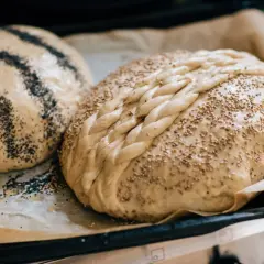 Två hembakade bröd, ett med vallmofrön och ett flätat med sesamfrön, redo att baka och frysa in.