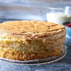 En fluffig sockerkaksbotten, redo att bli en del av ett anslag recept. Bredvid står en skål med sylt och en kanna med grädde.