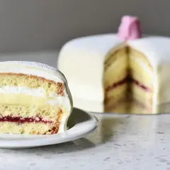 En skiva av en klassisk prinsesstårta med lager av sockerkaka, vaniljkräm, vispgrädde och hallonsylt. Perfekt för ett prinsesstårta recept.