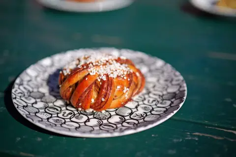 En gyllene kanelbulle med pärlsocker på en mönstrad tallrik. Perfekt för fika, kanske inspirerad av ett enkelt kanelbullar recept.
