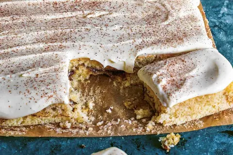 En saftig sockerkaka med krämig glasyr och ett generöst strössel av kanel. En bit saknas, redo att avnjutas.