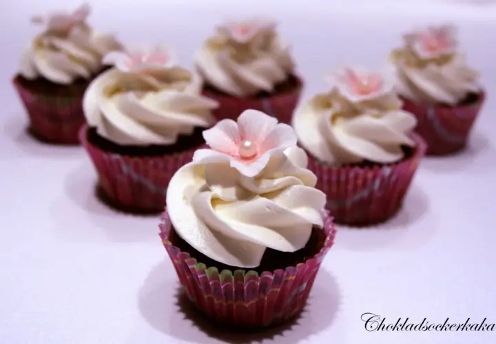 Sju små mini cupcakes med vit frosting och rosa blommor. Perfekta för ett sött kalas.