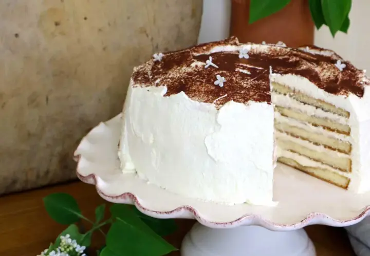 En vacker tiramisu tårta med lager av kräm och kex, toppad med kakao och små vita blommor.