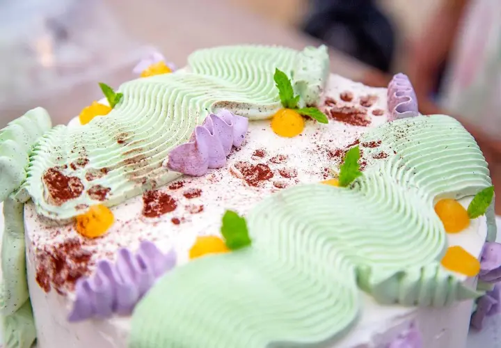 En vacker jordgubbsmousse tårta med grön och lila frosting, toppad med aprikoser och myntablad.