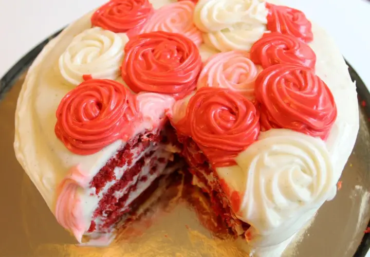 En saftig red velvet-tårta med lager av rött och vitt fluffigt frosting, dekorerad med rosformade frostingblommor i rött och vitt.