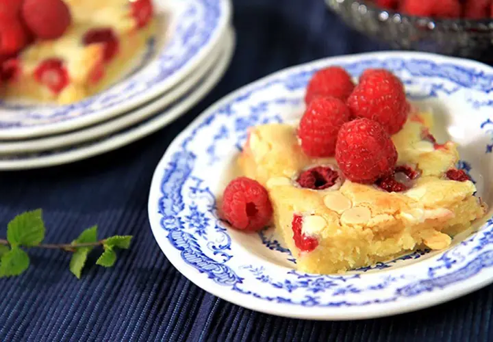 En bit hallonblondie på en blåvit tallrik, perfekt för ett somrigt blondie recept.
