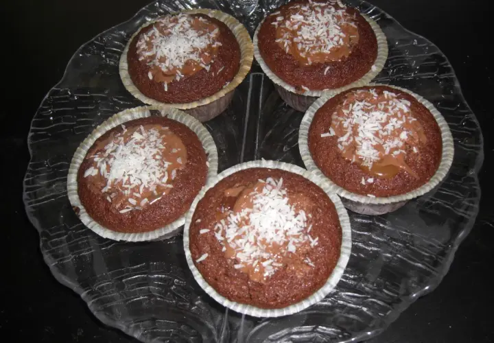 Fem kladdkakemuffins med kola och kokosflingor på ett glasfat.