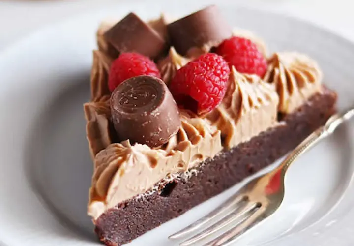 En bit kladdkaka med fluffig chokladfrosting, toppad med hallon och chokladbitar. En perfekt kombination för alla chokladälskare.