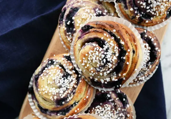 Nybakade blåbärsbullar med pärlsocker på en träbricka, redo att avnjutas.