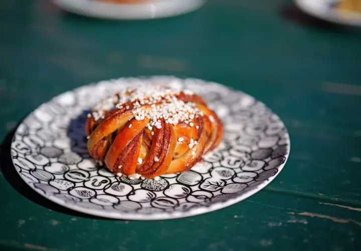 En gyllene kanelbulle med pärlsocker på en mönstrad tallrik. Perfekt för fika, kanske inspirerad av ett enkelt kanelbullar recept.