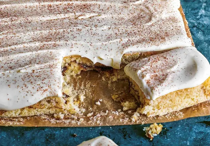 En saftig sockerkaka med krämig glasyr och ett generöst strössel av kanel. En bit saknas, redo att avnjutas.
