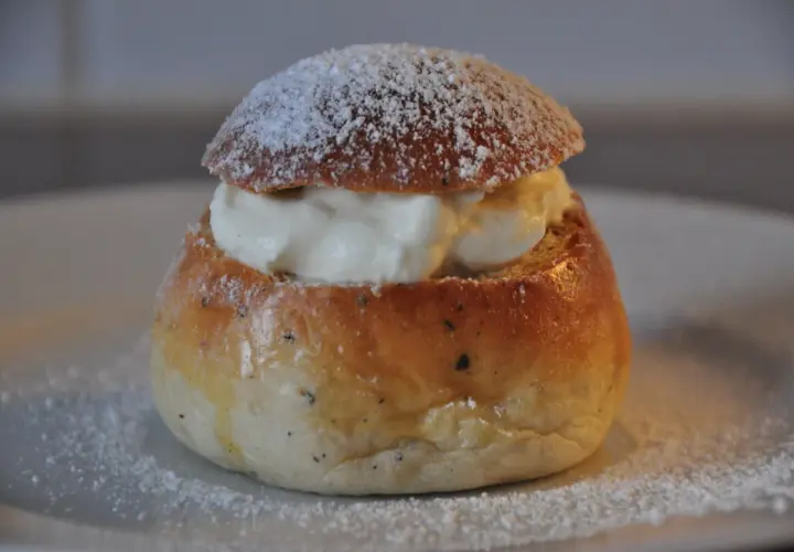 En nybakad semla, redo att avnjutas. Den gyllene bullen är fylld med fluffig grädde och pudrad med florsocker. Perfekt för att baka semmelbullar.