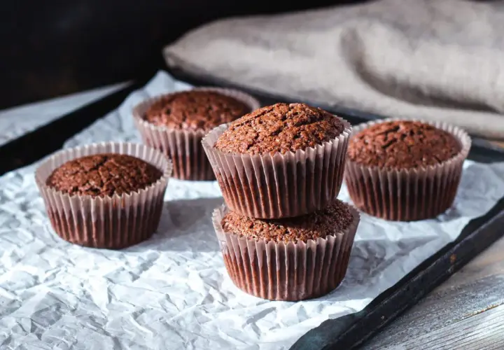 Fem choklad cupcakes i pappersformar, staplade och utspridda på vitt papper.