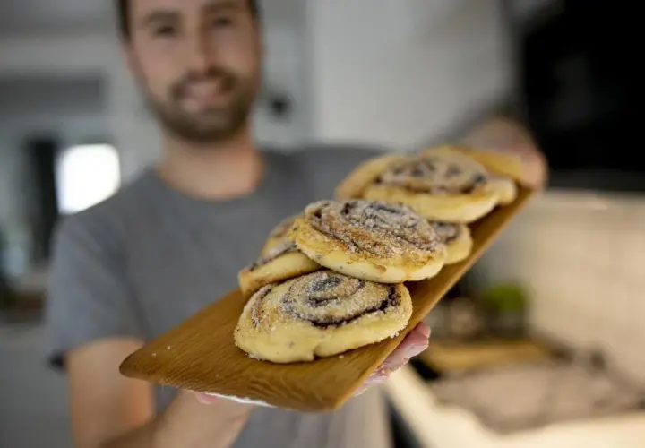Man håller fram en bricka med nybakade kanelbullar utan ägg, strösslade med socker.