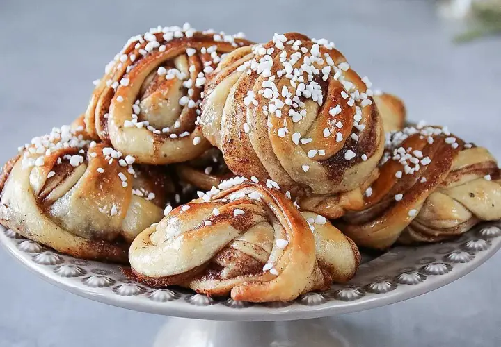 En hög med laktosfria kanelbullar, toppade med pärlsocker, ligger på ett fat.