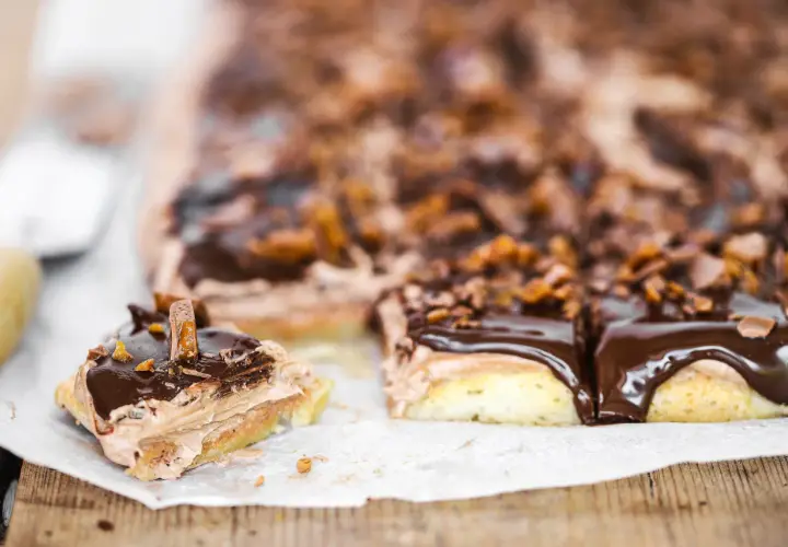 Mäktiga mjuka kakor i långpanna med chokladglasyr och krispiga bitar. En bit är uppskuren och visar lager av fluffig kräm.