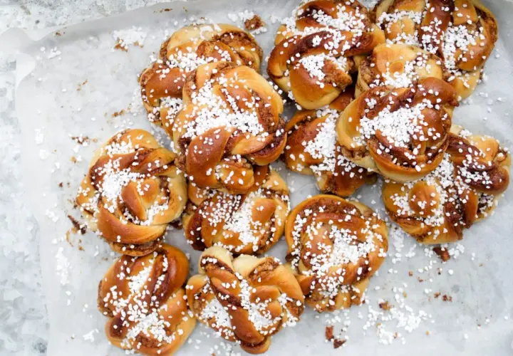 En hög med gyllene kanelbullar, toppade med pärlsocker. Perfekt för en fika, dessa sukat frukt-inspirerade bakverk doftar ljuvligt.