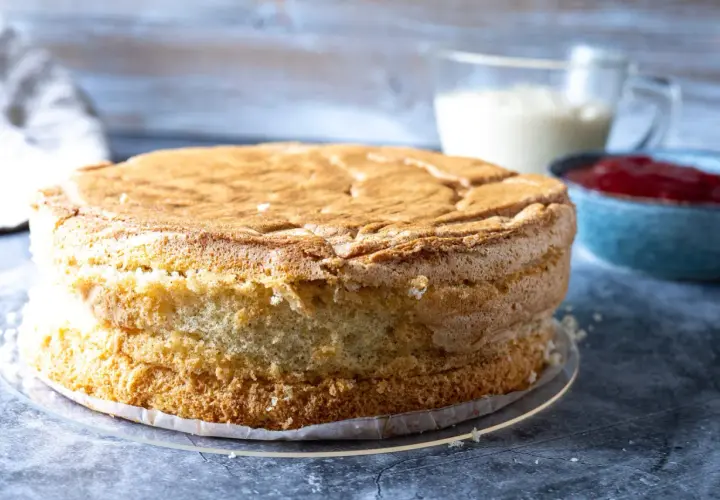 En fluffig sockerkaksbotten, redo att bli en del av ett anslag recept. Bredvid står en skål med sylt och en kanna med grädde.