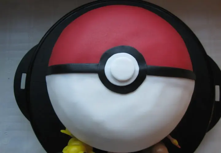 En fantastisk pokemon tårta formad som en pokéboll, med små pokemonfigurer som tittar fram.