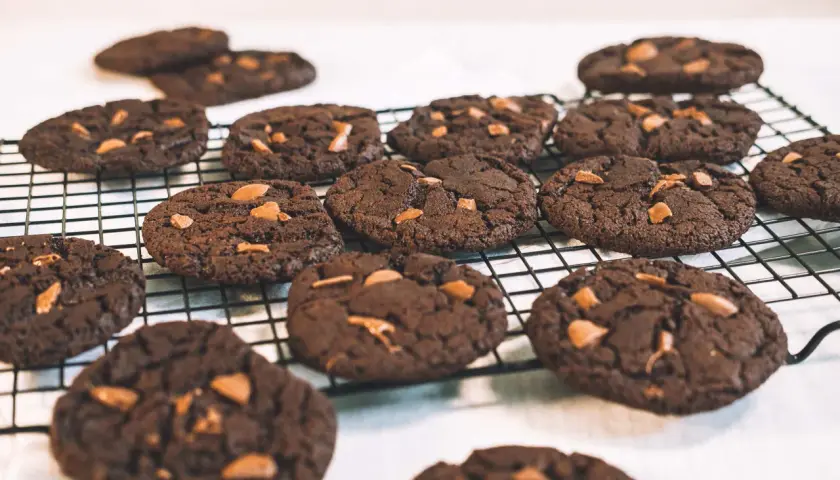 Många mörka, veganska chocolate chip cookies med chokladbitar ligger på ett svart galler.