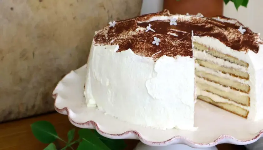 En vacker tiramisu tårta med lager av kräm och kex, toppad med kakao och små vita blommor.