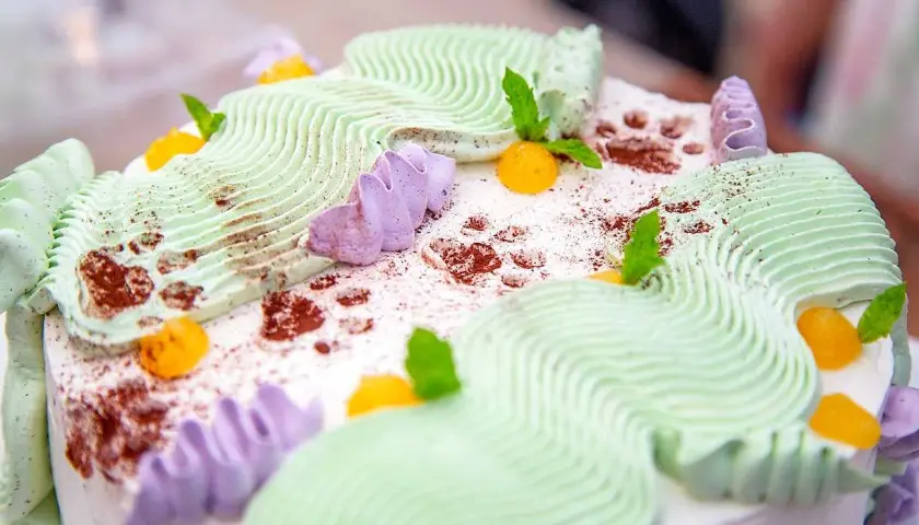En vacker jordgubbsmousse tårta med grön och lila frosting, toppad med aprikoser och myntablad.