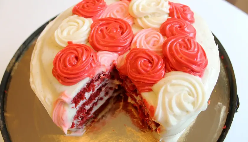 En saftig red velvet-tårta med lager av rött och vitt fluffigt frosting, dekorerad med rosformade frostingblommor i rött och vitt.
