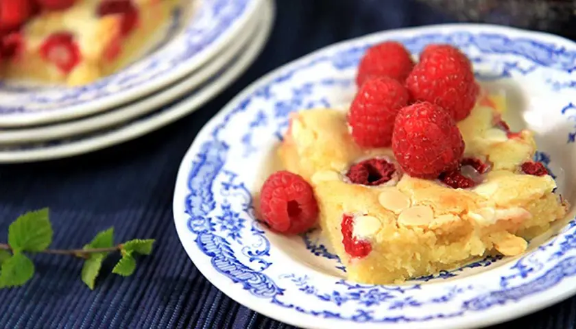 En bit hallonblondie på en blåvit tallrik, perfekt för ett somrigt blondie recept.