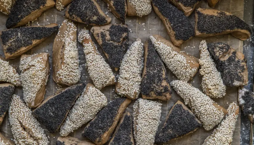 En bakplåt full med bröd som jäsa deg, täckta med sesamfrön och vallmofrön.
